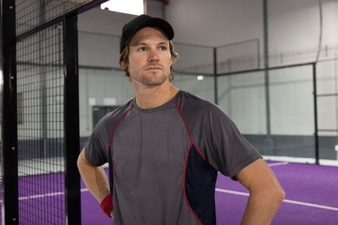 Focused male athlete standing on indoor padel court wearing cap and red wristband