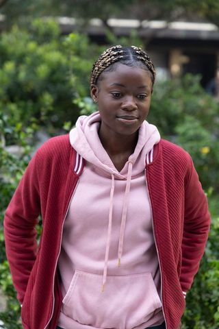 Young african american woman standing in courtyard wearing pink hoodie and maroon jacket