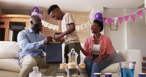 African American family celebrating birthday father giving gift while son opens present