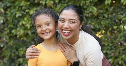 Mother and daughter smiling and embracing in sunlit backyard family portrait