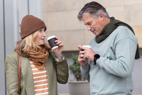 Middle-aged couple sharing coffee on urban street wearing casual autumn fashion and smartwatch