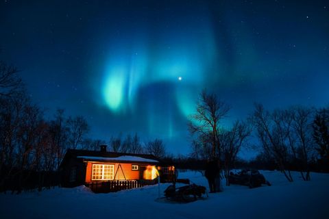 Cozy Cabin Under Vibrant Northern Lights in Night Sky