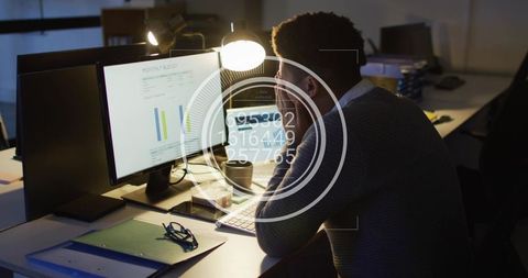 Man analyzing finance charts on dual monitors at night with futuristic hud data overlay