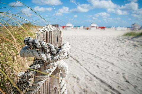 Weathered Rope Wrapping Wooden Post by Sand Dune with Lifeguard Chairs in Background