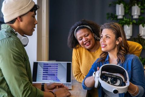 Diverse team demonstrating VR headset with data visualization on laptop in modern workspace