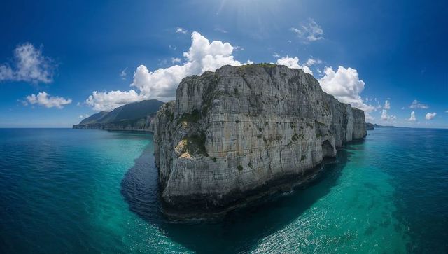 Towering limestone sea stack over turquoise ocean revealing sea caves and sunlit cliffs