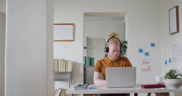 Man with headphones working on laptop in stylish home office environment, ideal for illustrating concepts related to remote work, technology, and productivity. This can be used for articles or advertisements about work-from-home setups, freelance work, and modern office designs.