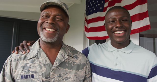 Father in military uniform smiles with son, with an American flag in background. Ideal for themes of family bond, patriotism, military service, and celebrations.