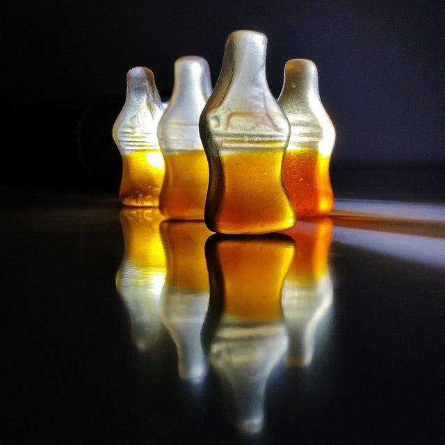 Close-up shot showing gummy cola bottle candies with light reflecting on them, creating a vibrant effect. Useful for food art, confectionery visuals, dessert menus, or candy promotions.