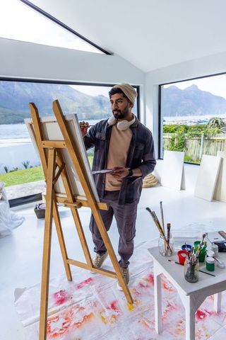 Artist painting at easel in bright waterfront studio with mountain view and minimalist