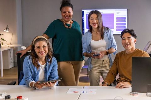 Diverse team collaborating in modern office presentation with laptop tablet and charts