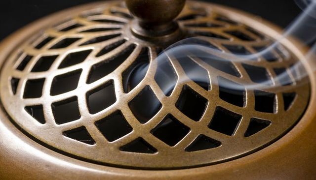 Curling smoke rising through antique bronze lattice lid with ornate central knob