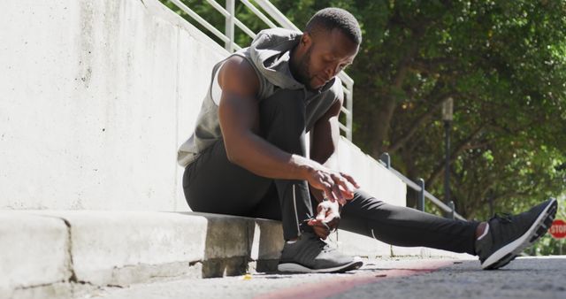 Athletic man tying shoelaces outdoors in urban area, preparing for run. Ideal for depicting fitness, sports preparation, active lifestyle, and urban workouts. Suitable for blog posts, health and fitness articles, advertisements for sports attire, and motivational content.