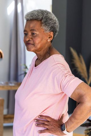 Senior african american woman standing in bright home wearing pink t-shirt and smartwatch