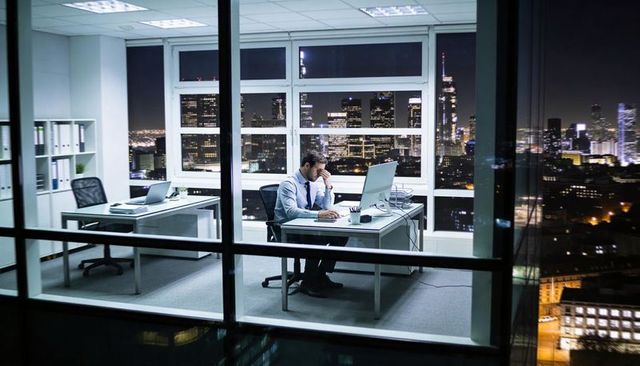 Late-night executive working alone in high-rise office overlooking lit city skyline