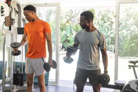 Two african american men performing dumbbell workout together in sunlit home gym