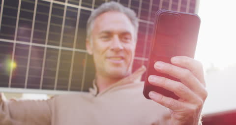 Smiling Man Holding Solar Panel Using Smartphone at Home