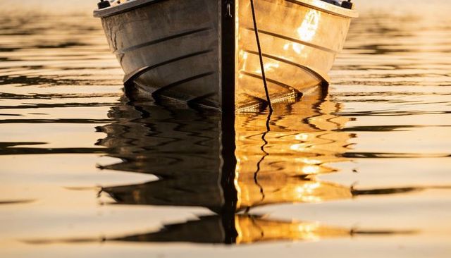 Aluminum boat bow reflecting golden sunset on rippling lake water with mooring rope