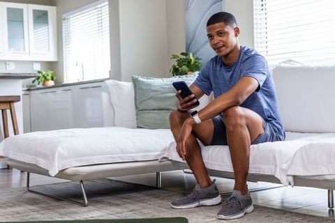 Young man checking smartwatch while using smartphone on modern minimalist sofa