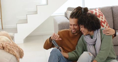 Young couple relaxing on living room floor sharing smartphone and smiling together