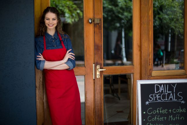 Portrait of smiling waitress standing with arms crossed outside the cafÃ©