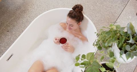 Woman Relaxing in Bubble Bath with Tea, Surrounded by Greenery