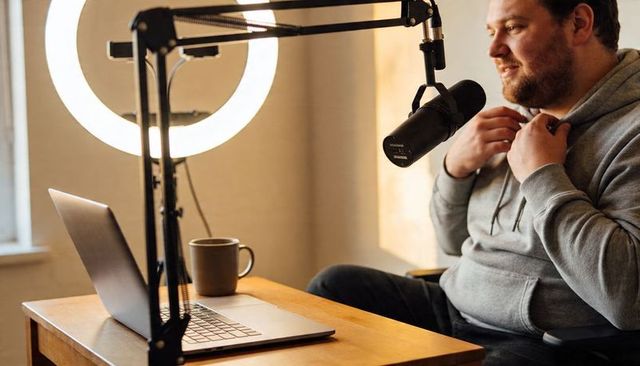 Adjusting microphone and prepping podcast setup in cozy home studio with ring light, laptop