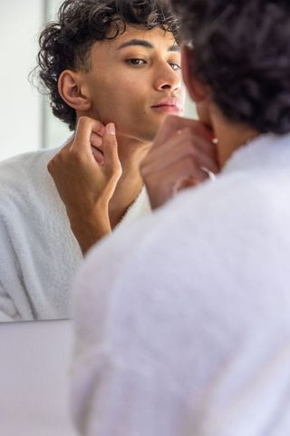 Young man examining jawline in bathroom mirror for skincare routine