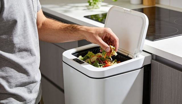 Man placing vegetable scraps into modern touchless white kitchen bin with black liner
