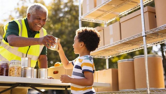 Senior volunteer handing canned food to child at outdoor community food bank