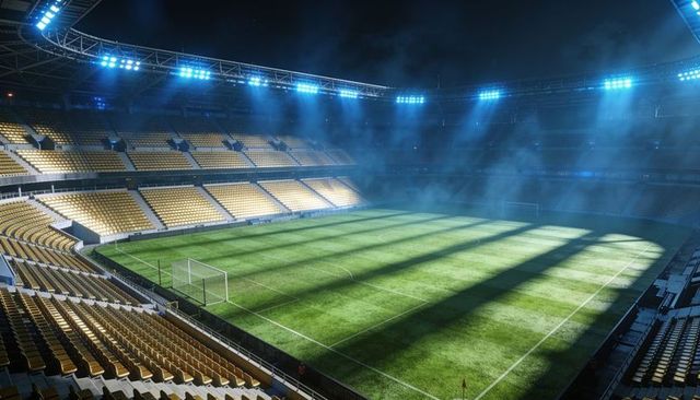 Floodlights illuminating football stadium at night with yellow stands and striped pitch