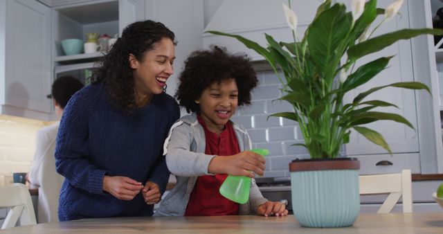 Biracial lesbian couple and daughter watering plants in kitchen. self isolation quality family time at home together during coronavirus covid 19 pandemic.