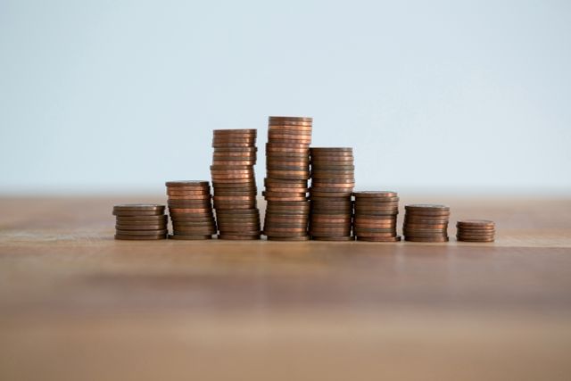This image shows neatly stacked coins on a wooden table, representing financial growth, savings, and investment. Ideal for use in financial blogs, banking advertisements, investment guides, and educational materials about money management.