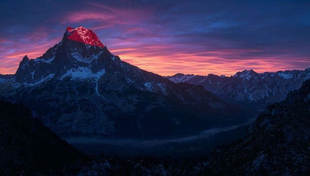 Alpenglow on Rugged Mountain Summit at Sunrise over Misty Alpine Valley Panorama