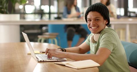 African american man smiling and typing on laptop in sunlit modern coworking coffeehouse