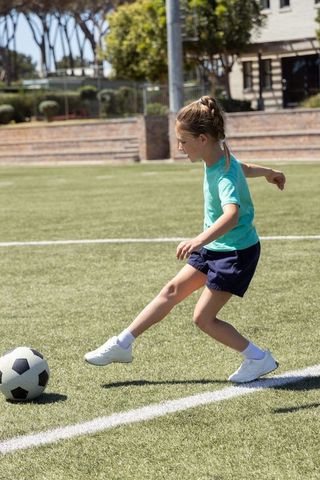 School-age girl kicking soccer ball on turf sideline during sunny youth practice