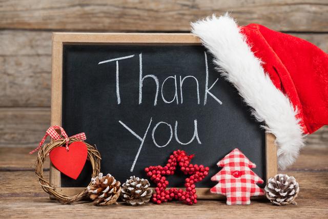 Chalkboard with 'Thank You' message adorned with Christmas decorations including a Santa hat, pine cones, and red and white ornaments. Ideal for holiday greeting cards, festive thank you notes, and seasonal social media posts.