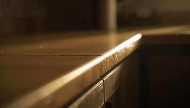 Sunlit wooden kitchen countertop edge with beveled joint and droplets sparkling on grain
