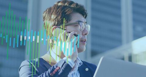 Asian executive talking on phone holding laptop with digital waveform business overlay