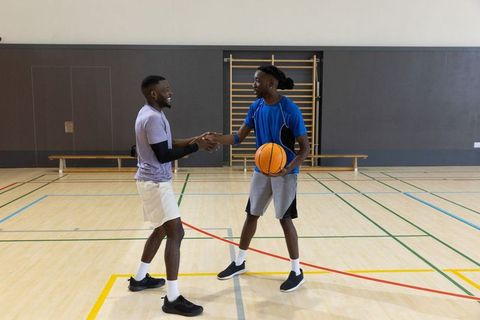 African american men shaking hands while holding basketball on gym court showing teamwork