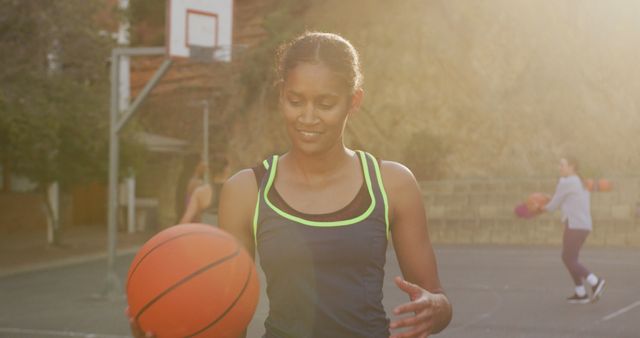 Woman practicing basketball outdoors at sunset, ideal for illustrating sports, fitness, determination, and active lifestyle concepts. Can be used in advertisements for sportswear, fitness programs, or motivational content.