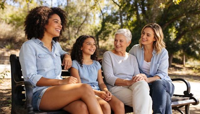 Multigenerational women smiling on park bench enjoying sunny day family bonding across generations