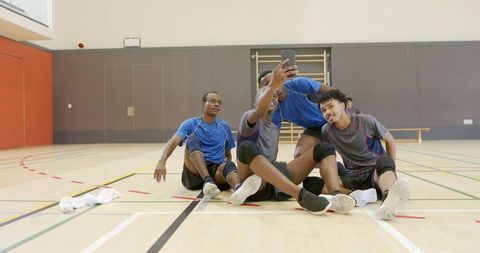 Diverse male volleyball teammates taking smartphone selfie on gym floor after practice