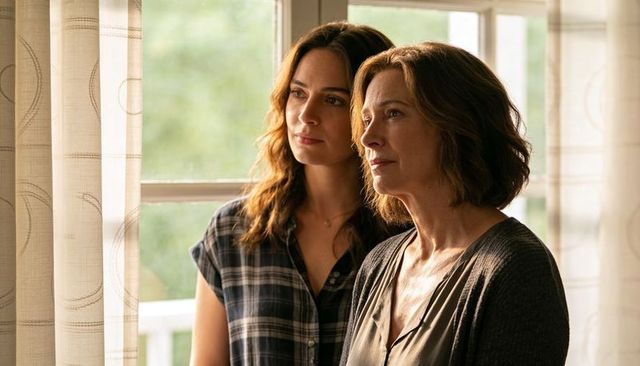 Mother and adult daughter gazing through window, warm natural light, intimate moment