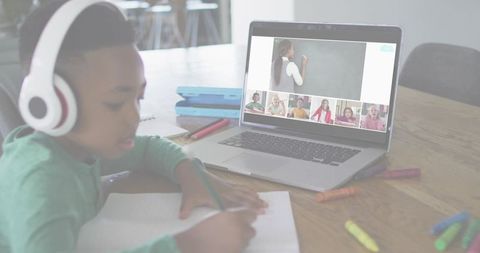 Boy in Headphones Learning Online Writes Down While Teacher Leads Class