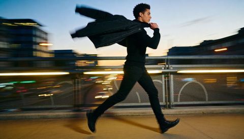 Urban runner sprinting across footbridge at dusk with coat flaring and motion trails