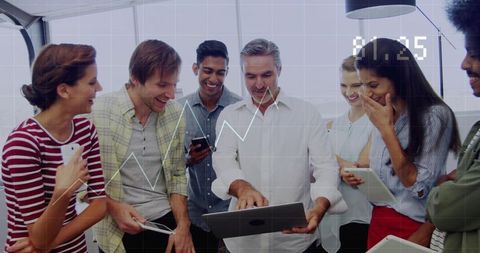 Diverse team collaborating around laptop in office with tablets and smartphones analyzing data