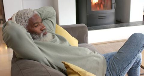 Senior Man Relaxing on Sofa in Cozy Living Room Near Wood-Burning Stove
