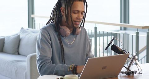 African american creator podcasting in modern living room with laptop and microphone