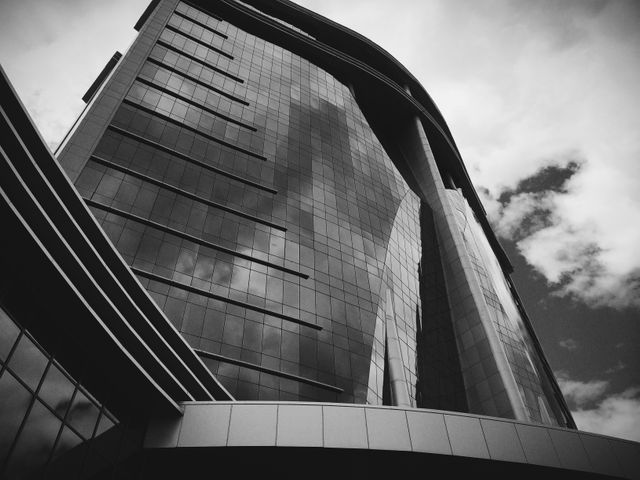 A striking view of a modern skyscraper with a reflective glass façade in black and white. Ideal for use in business presentation backgrounds or urban design themes. Perfect for illustrating concepts of modern architecture, urban development, or contemporary commercial real estate.